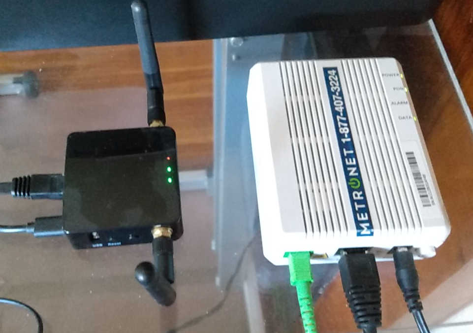 black mini-router with two attenna and white ONT box sitting on clear plexiglass table