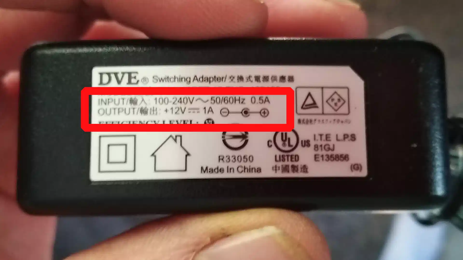 hand holding a power adapter with the rear label visible